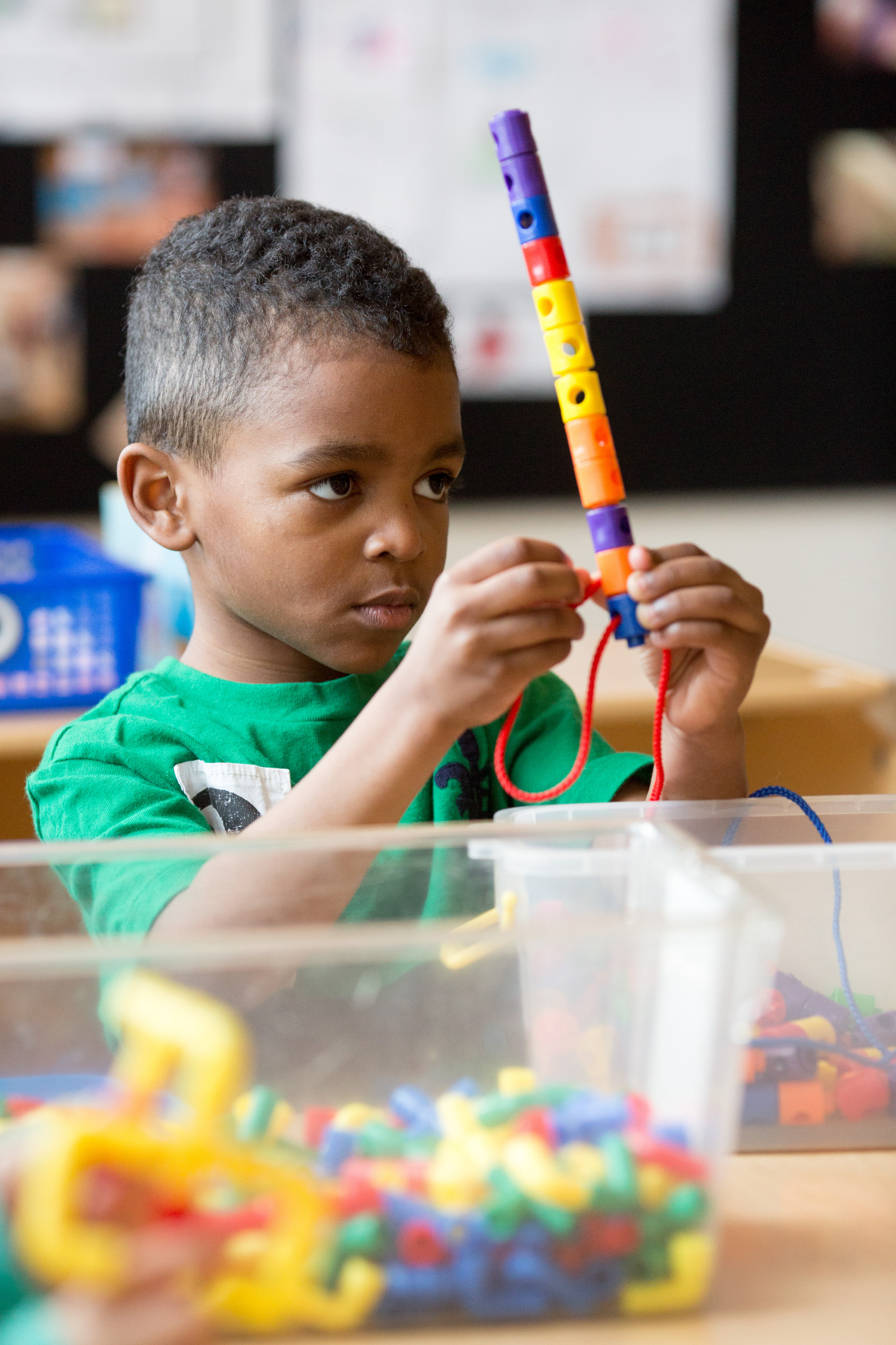 A preschool student threads plastic beads on a string.